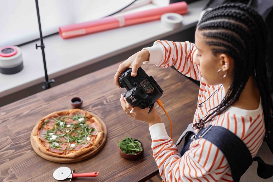 A creator photographing a rocket-topped pizza with a DSLR camera on a wooden restaurant table